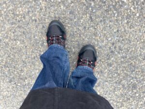 アスファルトの上、自分視点から撮った足元の画像。黒の本体に赤い靴紐が通されたウォーキングシューズ。